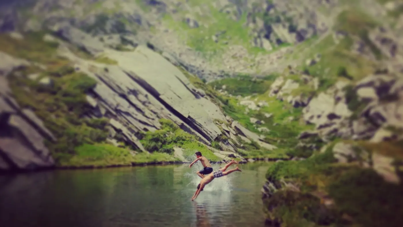 A young person leaping into a mountain lake beneath steep green crags