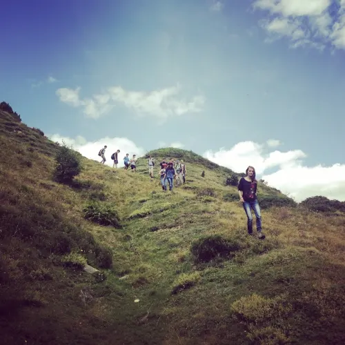 A group of young people walking down a grassy hillside under a big blue sky