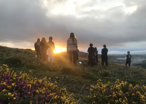 A group standing together on a hillside, silhouetted against the sunset